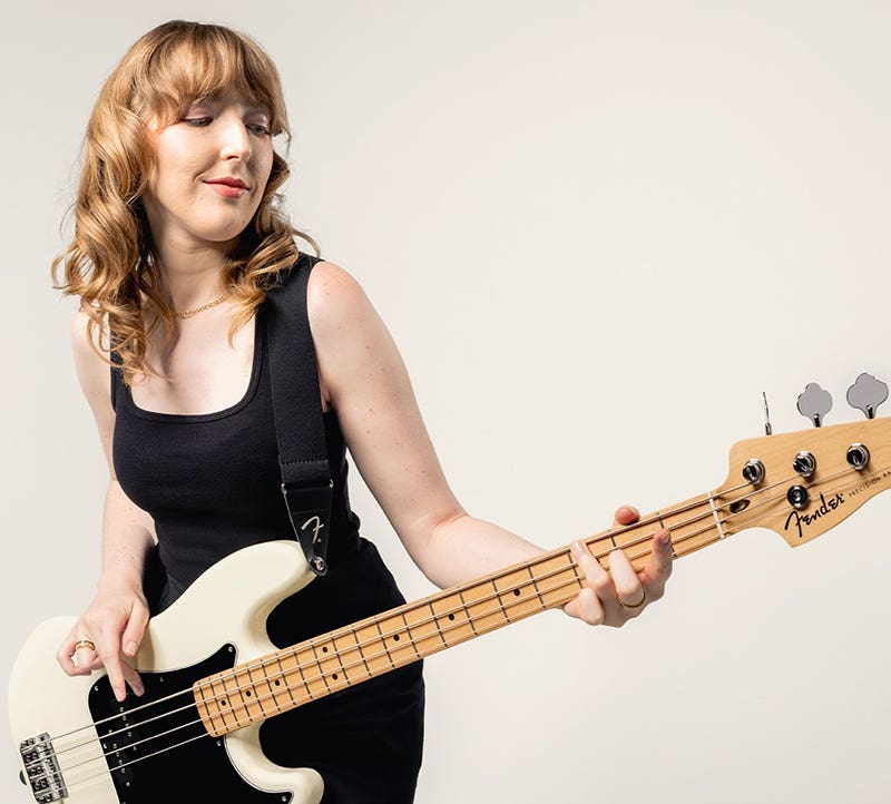 Woman playing a white Fender electric bass guitar against a plain background