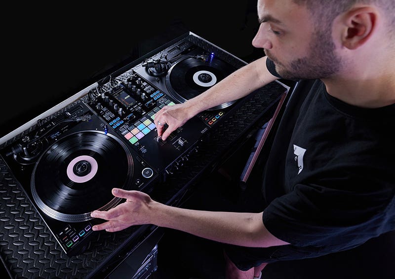 DJ performing with a professional dual turntable controller, adjusting vinyl platters and trigger pads during a live set.