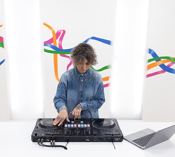 DJ performing on a controller with a laptop nearby and colorful abstract lines in the background.