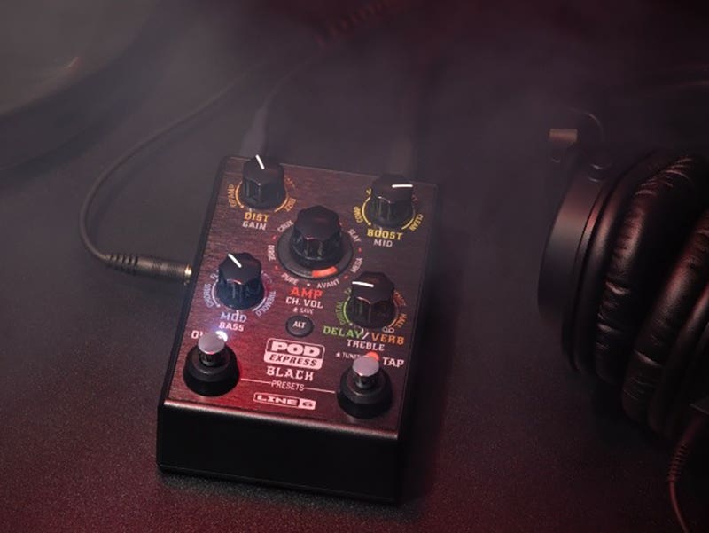 Close-up of a Line 6 POD Go guitar effects pedal surrounded by smoke, with headphones and guitar cables nearby.