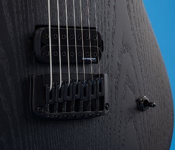 Close up on the strings of a Schecter 7-string guitar on a blue background.